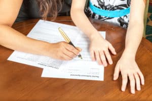 Woman with daughter signing a document.