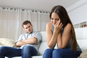 Woman lamenting domestic violence beside her angry husband sitting on a couch in the living room in a house indoor